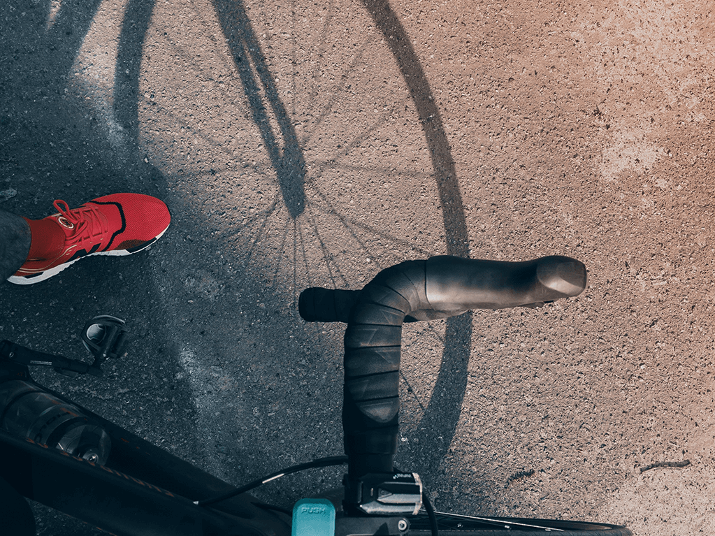 View from above a person with red shoes on a bike with the shadow of the wheel